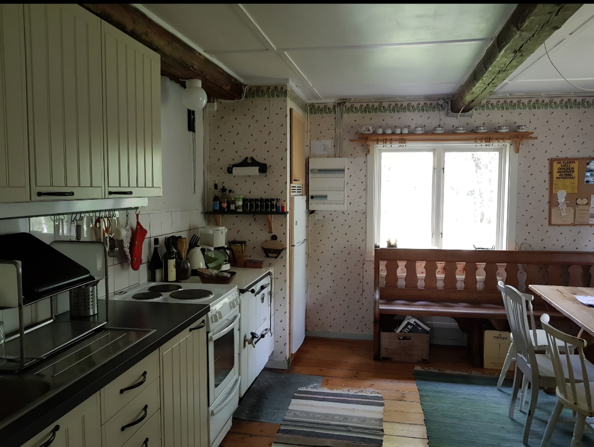 Köket med vita skåp, spis och bänk under fönstret