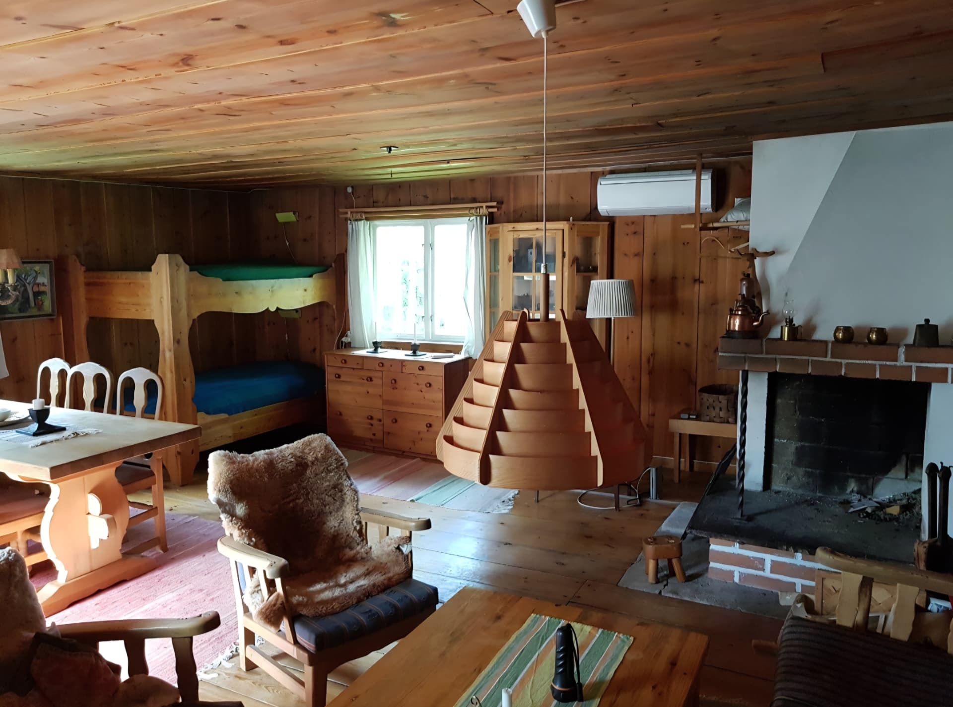 Storstugan med öppen spis, matbord och sittplatser i furu